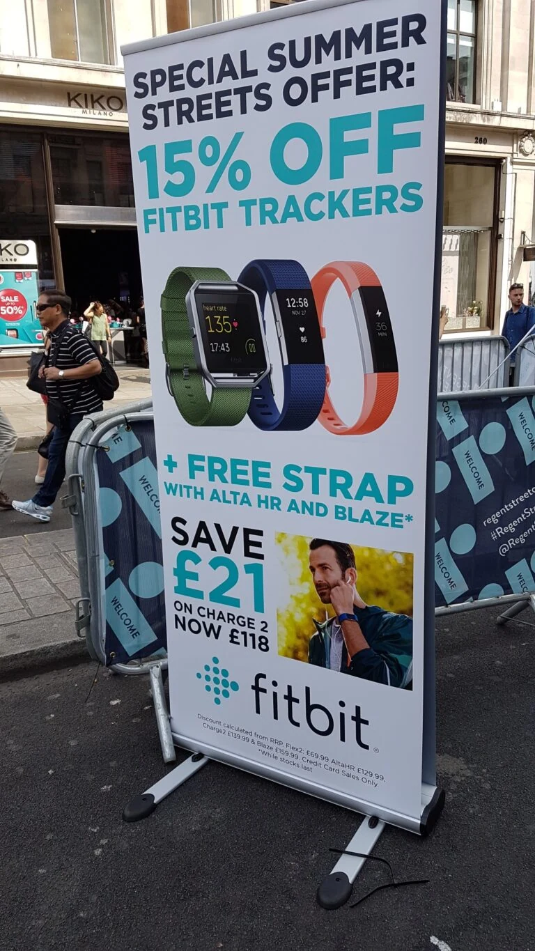 A Fitbit banner on Regent Street: “Special Summer Streets offer: 15% off Fitbit trackers”, showing three trackers and a free strap offer